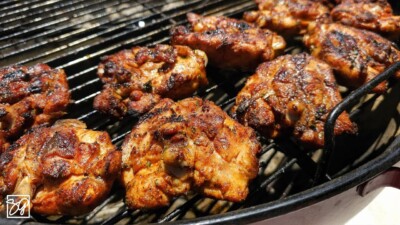 Several pieces of seasoned, grilled chicken are cooking on a barbecue grill, with char marks visible and golden-brown, crispy skin—perfect for those searching for delicious grilled chicken recipes.