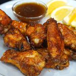 A plate of crispy honey lemon pepper wings with a small bowl of dipping sauce and lemon wedges on the side. The wings are golden brown and look flavorful, perfect for anyone seeking a delicious lemon pepper wings recipe.
