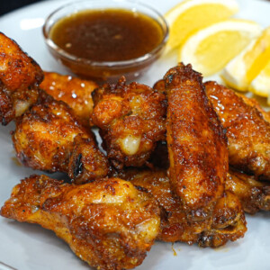 A plate of crispy honey lemon pepper wings with a small bowl of dipping sauce and lemon wedges on the side. The wings are golden brown and look flavorful, perfect for anyone seeking a delicious lemon pepper wings recipe.