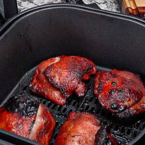 Four pieces of cooked, seasoned air fryer chicken thighs with crispy, browned skin rest inside an open air fryer basket on a kitchen counter.