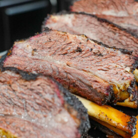 Close-up of several large, juicy smoked beef ribs arranged on a cutting board, showing a dark, charred bark on the outside and a tender, pink interior—a perfect example of how to smoke beef ribs to perfection.