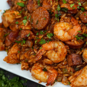 A close-up of a plate filled with jambalaya, featuring shrimp, sausage slices, rice, and chopped herbs on a white dish&mdash;perfect inspiration for trying new jambalaya recipes or finding an easy jambalaya recipe to make at home.