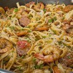 A close-up of a pan filled with creamy cajun shrimp pasta—fettuccine tossed with shrimp, sausage, diced tomatoes, and parsley, all topped with grated cheese for a classic cajun pasta recipe.
