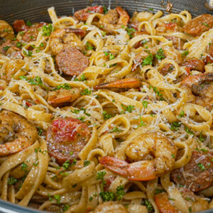 A close-up of a pan filled with creamy cajun shrimp pasta&mdash;fettuccine tossed with shrimp, sausage, diced tomatoes, and parsley, all topped with grated cheese for a classic cajun pasta recipe.