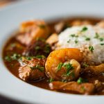A close-up of a plate of seafood gumbo topped with white rice, featuring shrimp, sausage, and vegetables in a rich, brown sauce—perfect for anyone craving an authentic gumbo or searching for the ideal seafood gumbo recipe.