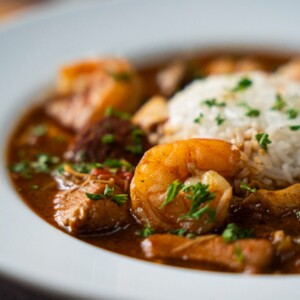 A close-up of a plate of seafood gumbo topped with white rice, featuring shrimp, sausage, and vegetables in a rich, brown sauce&mdash;perfect for anyone craving an authentic gumbo or searching for the ideal seafood gumbo recipe.
