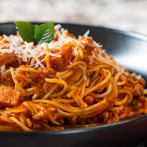 A close-up of a plate of spaghetti with tomato-based meat sauce, topped with grated cheese and fresh basil, served in a black bowl&mdash;perfect inspiration for your next spaghetti sauce recipe.
