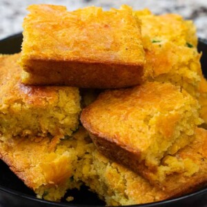 A black bowl filled with several golden-brown pieces of Mexican cornbread, stacked on top of each other, set on a marbled surface.