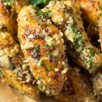 A close-up of crispy garlic parmesan chicken wings coated in a rich garlic parmesan wing sauce, topped with herbs and grated cheese. The golden brown wings are garnished with chopped parsley for a flavorful finish.