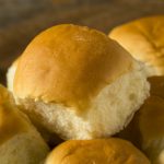A close-up of several golden brown, fluffy dinner rolls with a soft texture, stacked together on a wooden surface—perfect inspiration for your next dinner roll recipe.