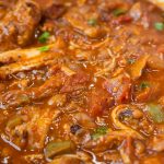 A close-up of a hearty, thick Cajun chili with shredded meat, beans, tomato chunks, and green onions in a rich, red sauce—a flavorful Cajun chili recipe perfect for any comfort food craving.