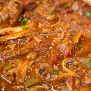 A close-up of a hearty, thick Cajun chili with shredded meat, beans, tomato chunks, and green onions in a rich, red sauce—a flavorful Cajun chili recipe perfect for any comfort food craving.