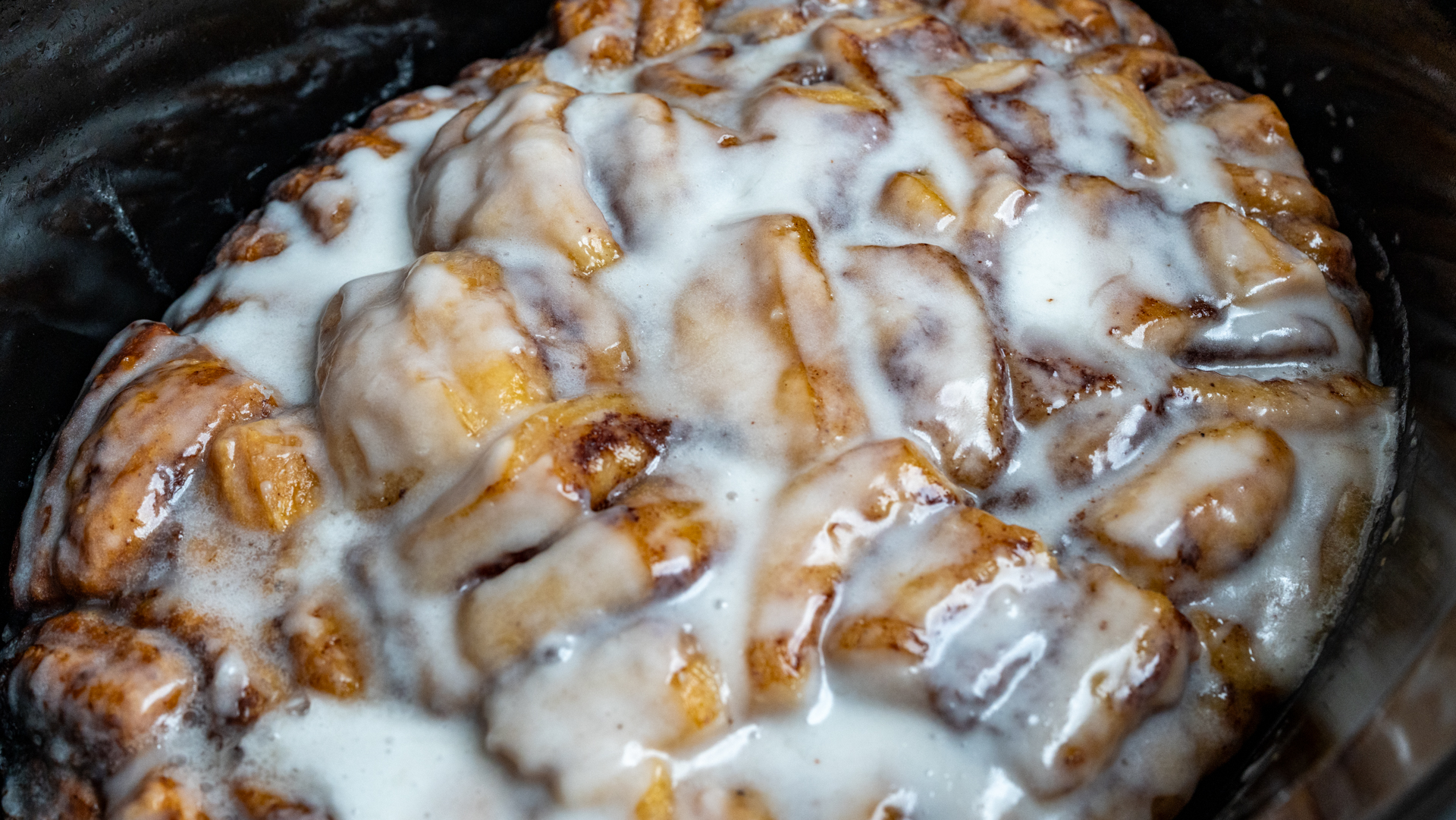 Cooked cinnamon roll casserole covered with icing in a slow cooker