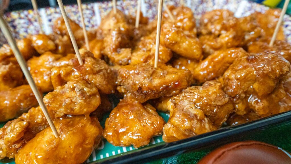 Close-up of glazed, golden-brown hot honey chicken bites on a tray, each piece skewered with a wooden toothpick for easy serving. The sauce gives the nuggets a shiny, appetizing appearance.