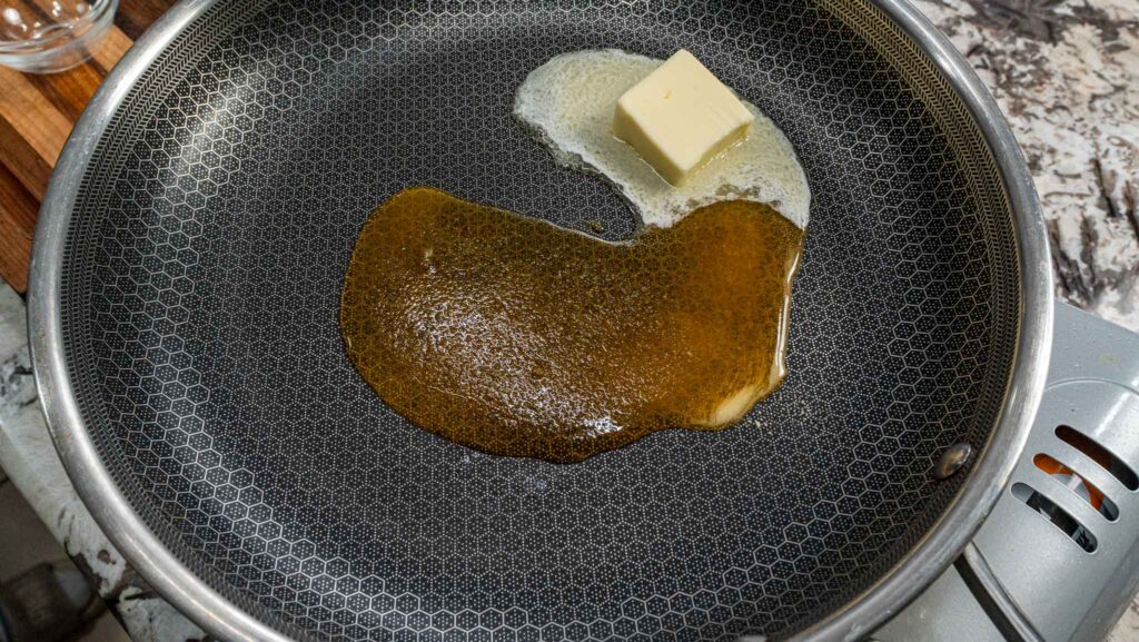 A piece of honey butter melting in a frying pan with a honeycomb pattern, forming a golden pool on the surface. The skillet is warming up on the stovetop, ready for cooking corn or your favorite dish.