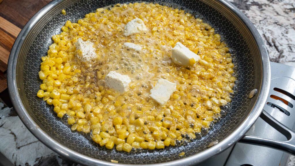 Corn kernels sizzle in a skillet with melting honey butter and a sprinkle of black pepper. Bubbling liquid surrounds the corn, infusing each bite with rich, sweet flavor as it cooks on the stovetop.