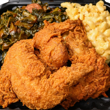 A black takeout container from Smokin and Grillin with AB Food Truck filled with crispy fried chicken, creamy macaroni and cheese, and cooked collard greens.