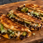 Three cheesy ground beef tacos with lettuce, chopped onions, pickles, and sauce are arranged in a row on a wooden cutting board. The taco shells are golden and slightly crispy.