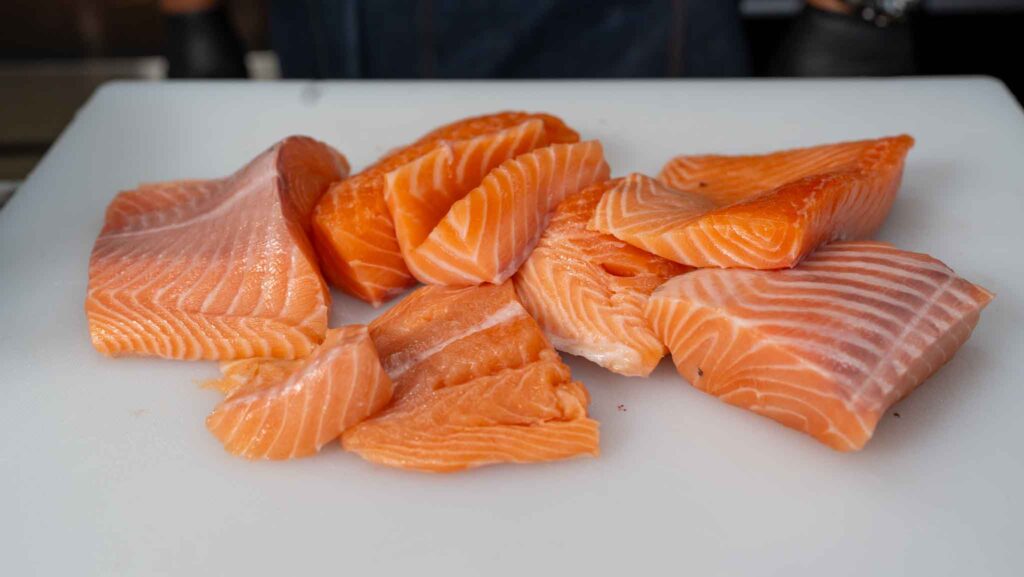 Several pieces of raw salmon with visible marbling are arranged on a white cutting board, perfect for making delicious salmon croquettes or preparing other flavorful dishes.