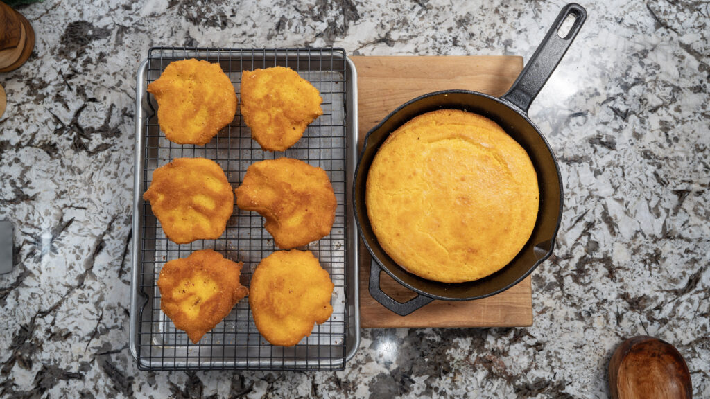 Golden cornbread muffins cool on a wire rack beside a classic cornbread baked to perfection in a cast iron skillet, all displayed on a granite countertop.