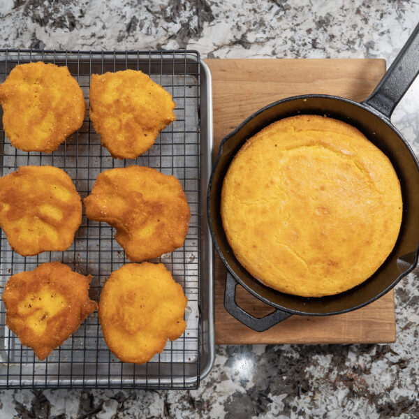 Golden cornbread muffins cool on a wire rack beside a classic cornbread baked to perfection in a cast iron skillet, all displayed on a granite countertop.