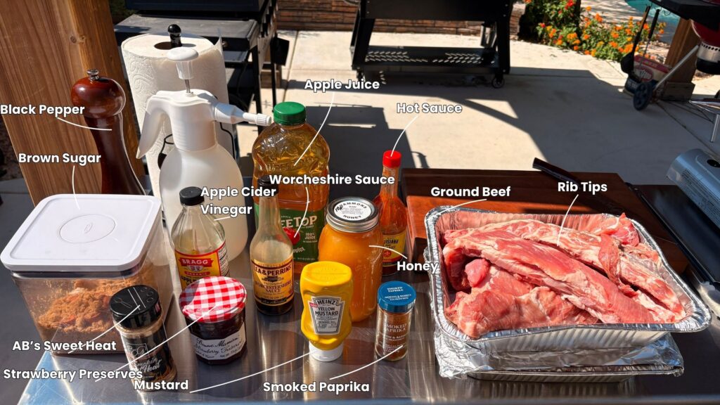 A table outdoors displays labeled Juneteenth BBQ rib tips and classic barbecue ingredients: black pepper, brown sugar, apple juice, hot sauce, ground beef, honey, Worcestershire sauce, apple cider vinegar, mustard, paprika, and strawberry preserves.