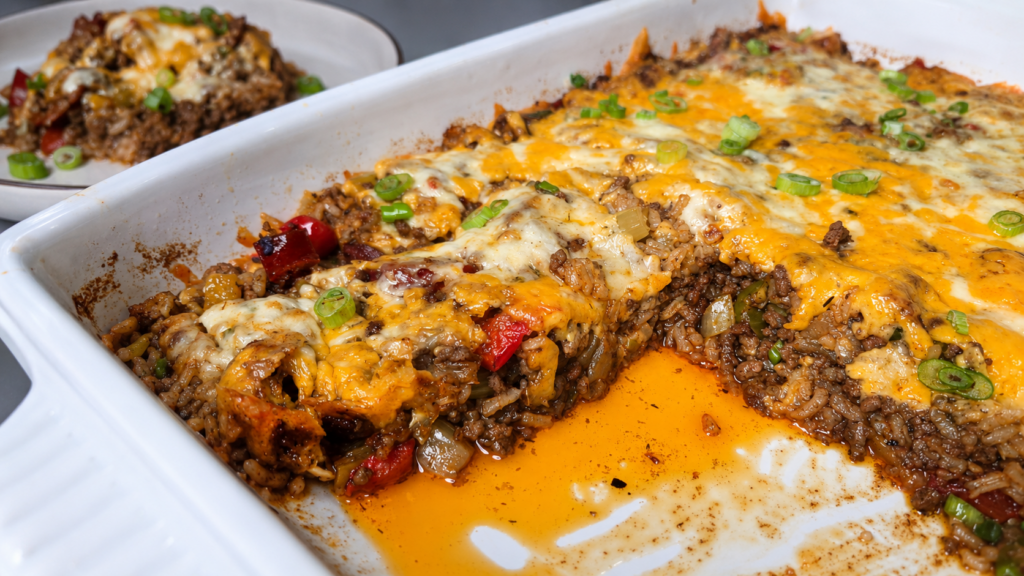 A cheesy ground beef casserole topped with melted cheese and chopped green onions, with a serving scooped out onto a plate in the background. Orange juices pool in the baking dish.