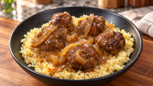 A black bowl filled with yellow rice topped with five meatballs in brown onion gravy, placed on a wooden surface.