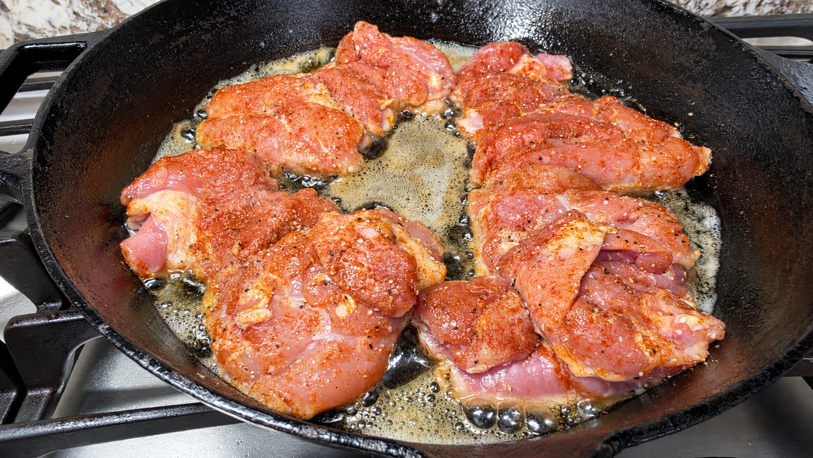 Seasoned chicken thighs beginning to sear in butter and oil in a cast-iron skillet.