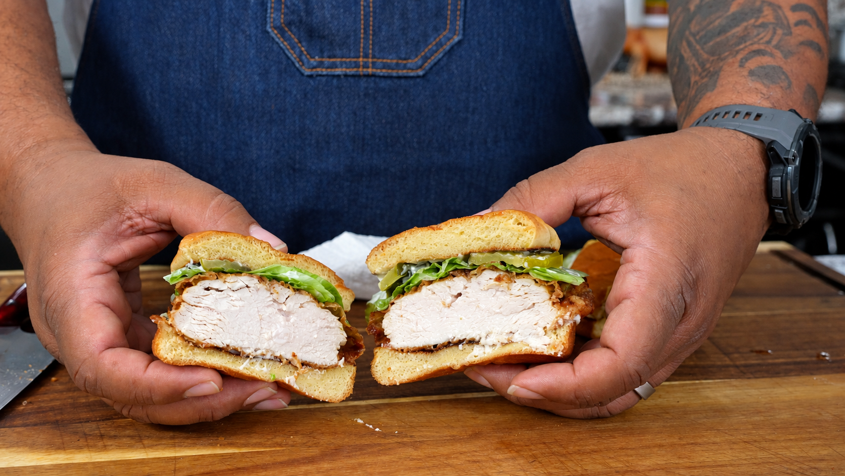 AB holding two halves of the finished fried chicken sandwich with lettuce and pickles
