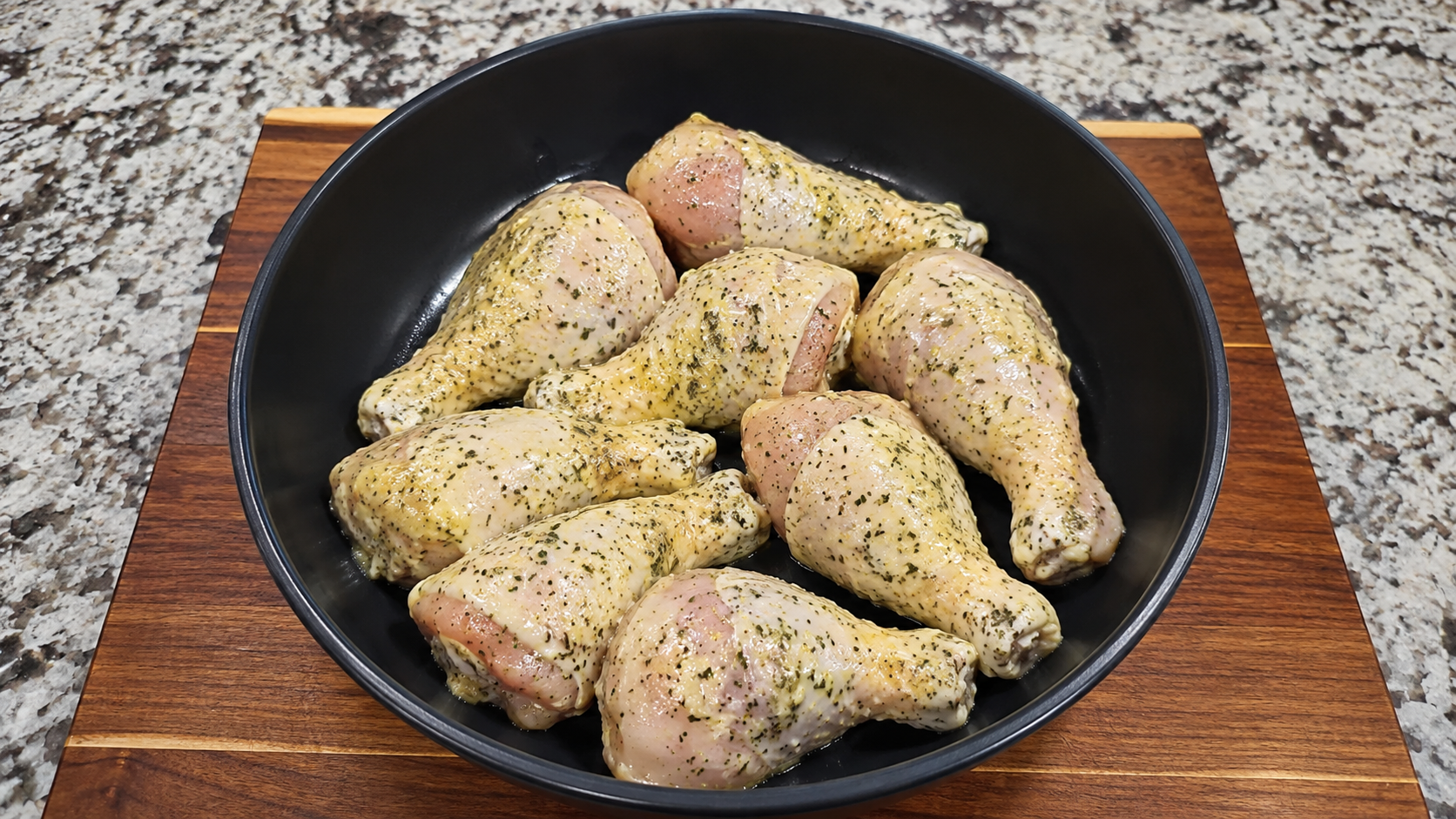 Raw chicken drumsticks coated in ranch-butter seasoning in a black bowl.
