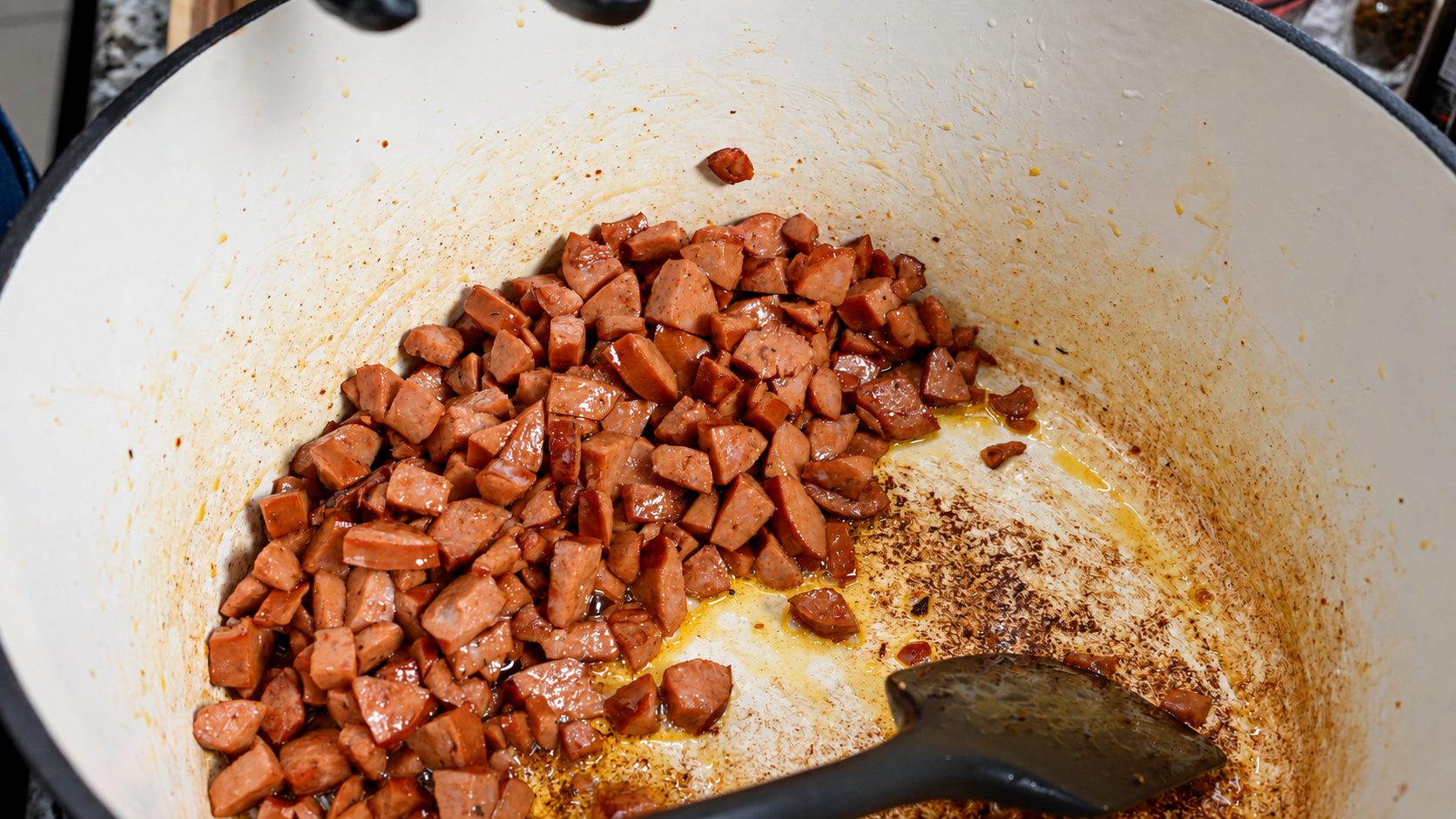 Diced smoked sausage browning in a white Dutch oven.