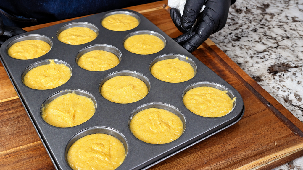 A muffin tin filled with yellow cornbread batter before baking.
