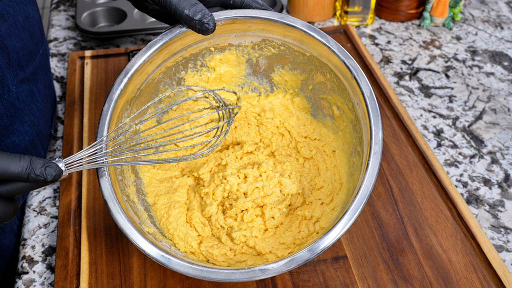 Cornbread batter mixed in a stainless steel bowl with a whisk.