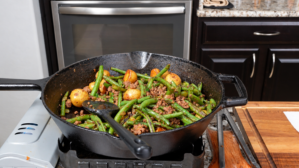 Cast iron skillet filled with dirty green beans, ground meat, and small roasted potatoes.