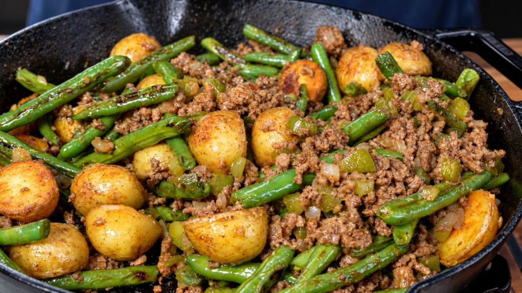 A cast-iron skillet filled with a sautéed mixture of ground meat, green beans, and golden roasted potatoes.