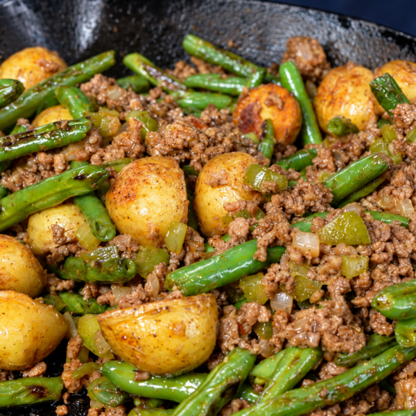 A cast-iron skillet filled with a sautéed mixture of ground meat, green beans, and golden roasted potatoes.