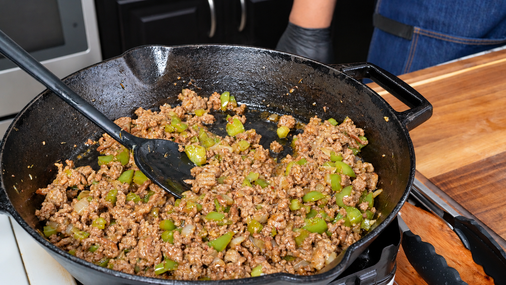Ground meat and chopped green peppers cooking in a cast-iron skillet for dirty green beans and potatoes.