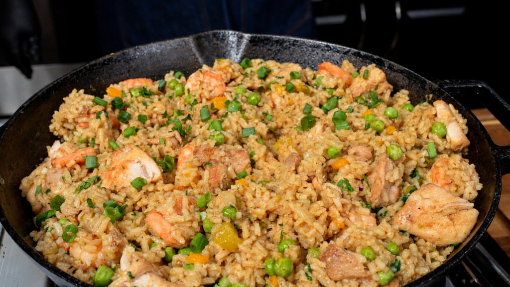 Cast iron skillet filled with chicken and shrimp fried rice topped with green onions and peas.