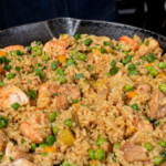 Cast iron skillet filled with chicken and shrimp fried rice topped with green onions and peas.