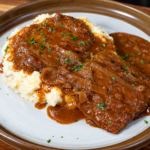 Smothered cube steak in onion gravy served over a bed of mashed potatoes.
