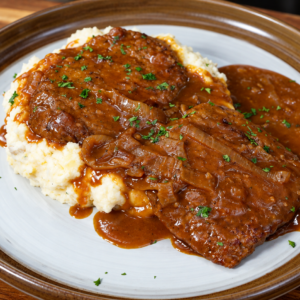 Smothered cube steak in onion gravy served over a bed of mashed potatoes.