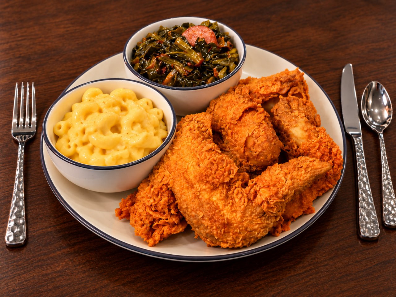 Crispy fried chicken with bowls of macaroni and cheese and cooked greens.