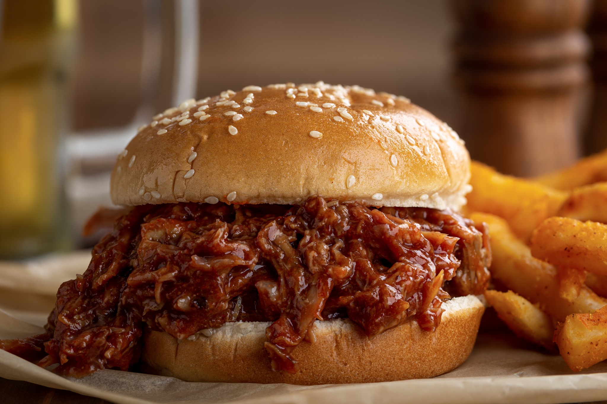 Sauced pulled pork sandwich on a sesame bun with potato wedges